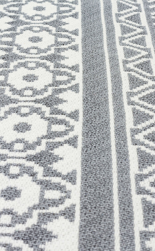 Load image 1 in gallery view. A close-up of the Grey Drift - Washable Reversible Kilims - AR07 rug, showcasing gray and white geometric and floral patterns with alternating stripes, inspired by tribal motifs.