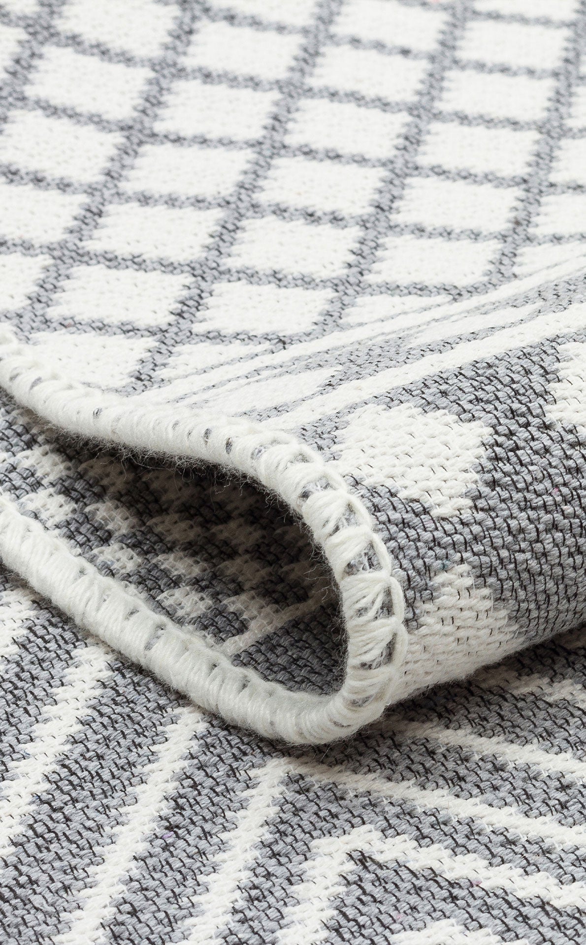 A close-up of the Grey Drift - Washable Double-Sided Kilims - AR07 shows its gray and white geometric patterns, thick stitched edge, and a slightly folded corner, highlighting the rug’s stylish washable design.