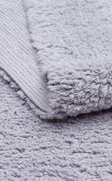 A close-up of the Grey Snug - Washable Shaggy (CBNPLAIN) rug shows its soft, textured light gray, fluffy pile with a slightly raised surface and a visible woven underside corner.