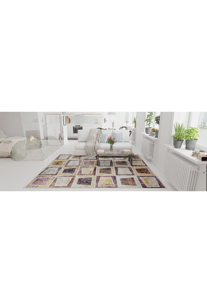 A bright, modern living room with white walls, large windows, indoor plants, a cozy couch, and the Gridiron Glow - Washable Rug - JR183 (Custom Size), featuring colorful geometric patterns that add warmth near a glowing fireplace.