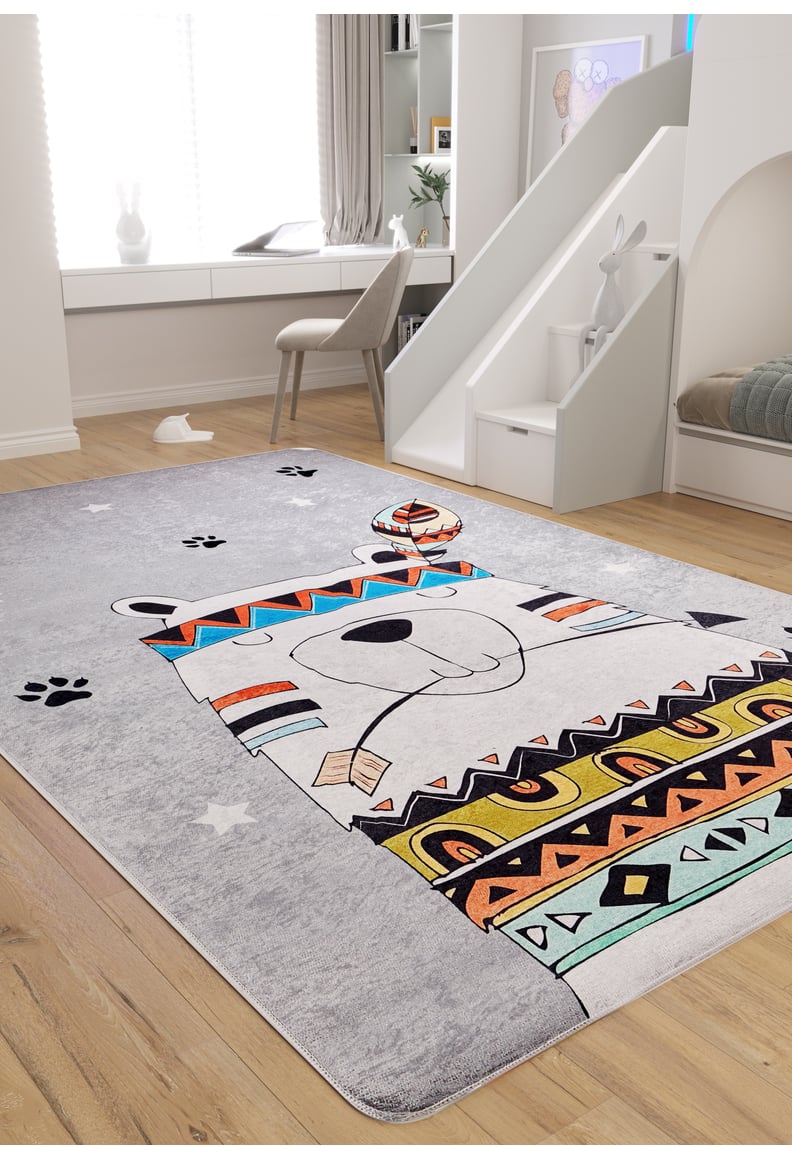 A kids' room with a slide and light wood flooring features the Groovy Bear - Machine-Washable Rug JRC093 in gray-anthracite, showcasing a cartoon bear with colorful tribal patterns and paw prints. A chair is by the window; a plush bunny rests on the slide steps.