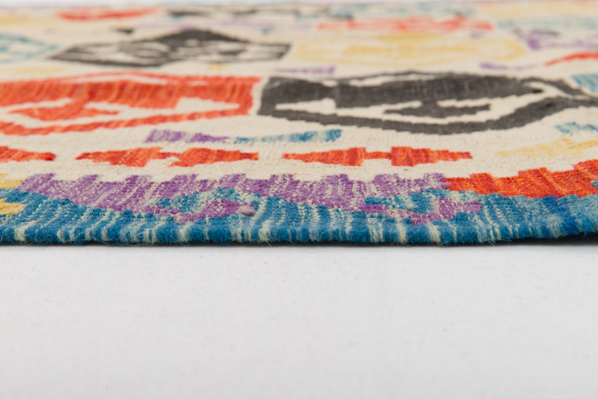 Close-up side view of the Handcrafted Story - Handwoven Kilim, showcasing its colorful geometric patterns in blue, purple, red, black, and cream. The image highlights the rug’s texture and thickness against a white background.