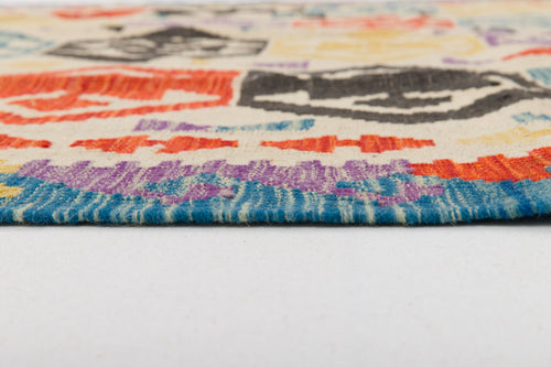 Load image 1 in gallery view. Close-up side view of the Handcrafted Story - Handwoven Kilim, showcasing its colorful geometric patterns in blue, purple, red, black, and cream. The image highlights the rug’s texture and thickness against a white background.