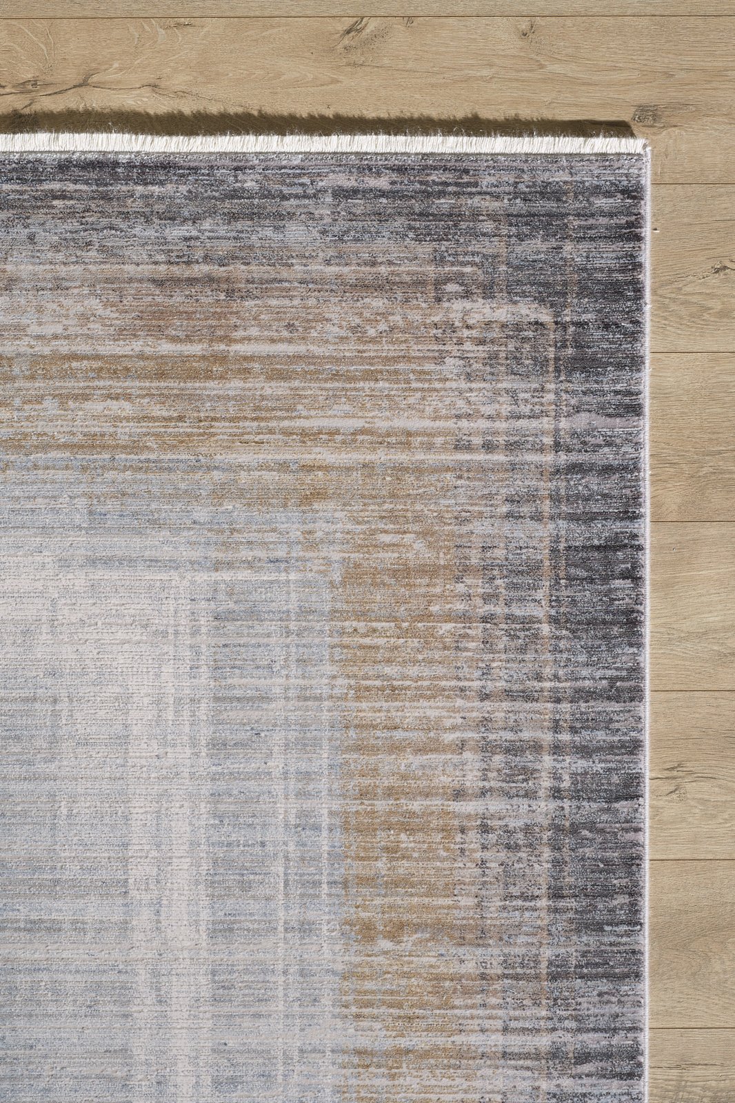 A detailed view of the Harmony in Contours Modern Bordered Rug - EW5743, a rectangular, machine-made rug with gradient gray, beige, and blue shades, subtle texture, and fringed edges placed on a light wood floor.