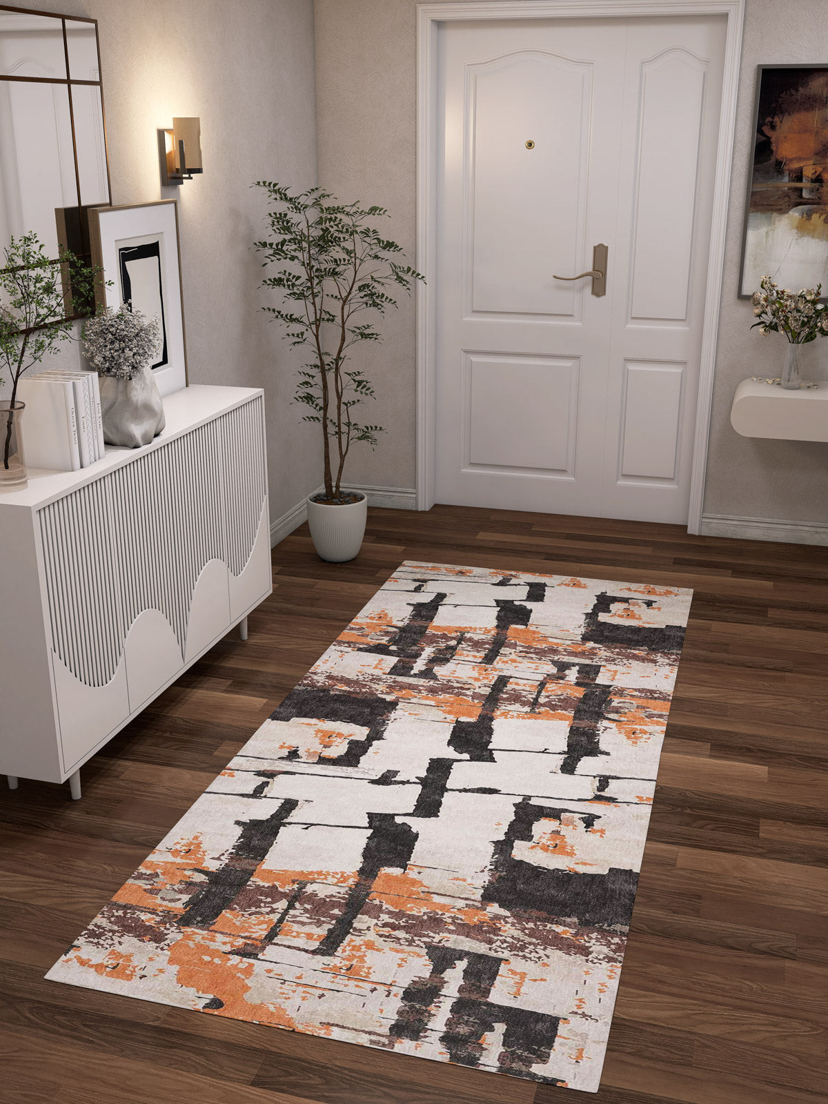 A modern hallway with a white door, wooden floor, potted plant, white sideboard, wall art, and the Heirloom Touch - Washable Rug - JRN42 in orange, brown, and white abstract patterns—ideal for stylish modern interiors.