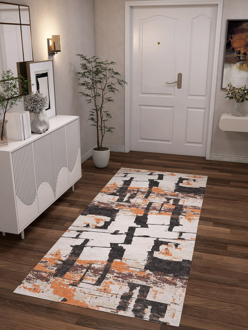 Load image 1 in gallery view. A modern hallway with a white door, wooden floor, potted plant, white sideboard, wall art, and the Heirloom Touch - Washable Rug - JRN42 in orange, brown, and white abstract patterns—ideal for stylish modern interiors.