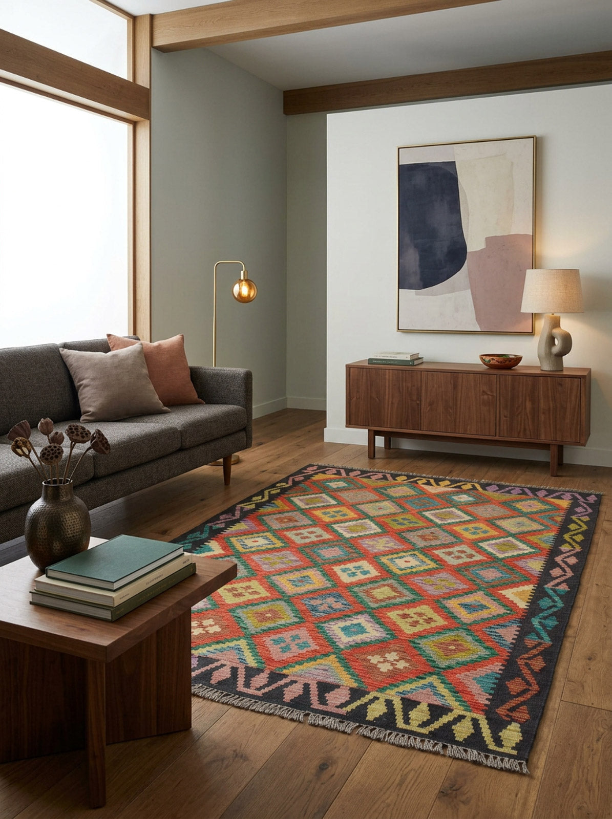 A modern living room features a gray sofa, wooden furniture, floor lamp, abstract wall art, and decor on a sideboard and table. The Heritage Weave - Handwoven Kilim adds color while a large window fills the space with natural light.
