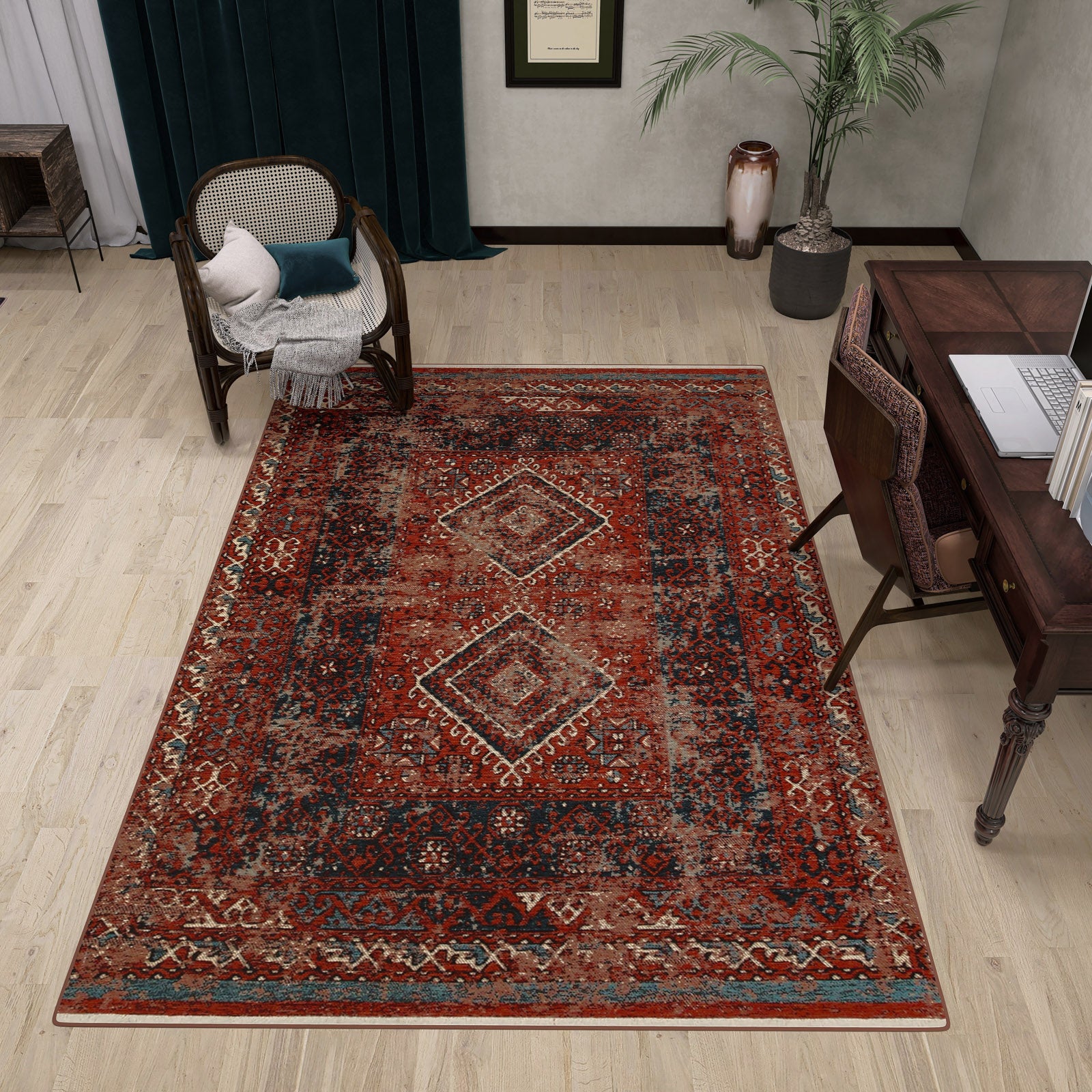 A cozy study with a large Heritage Blend - Washable Kilims - AND02 area rug in red and blue, a dark wooden desk and chair, a cushioned cane armchair, potted plants, dark green curtains, pale walls, and light wood flooring