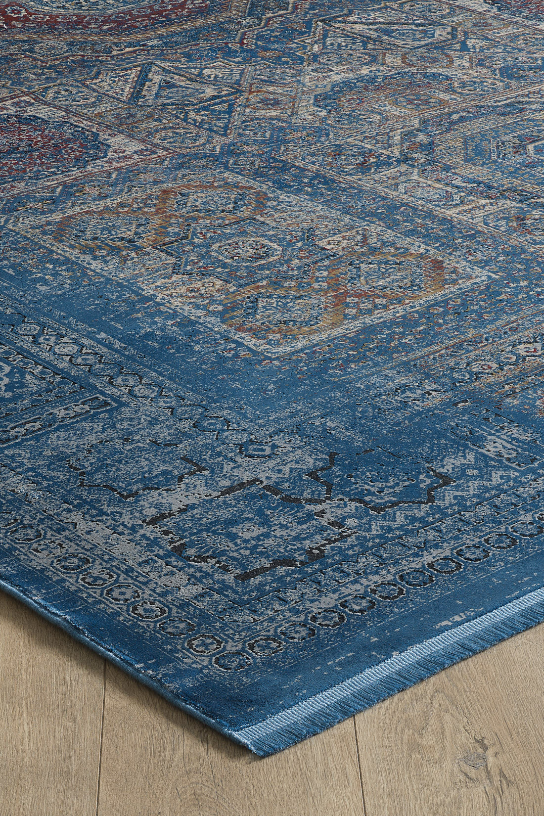 The Hidden Treasures Turkish Rug - Azure - 2223B, machine-made with intricate distressed blue, beige, and rust patterns, displays vintage geometric and floral designs and rests on a light wooden floor.