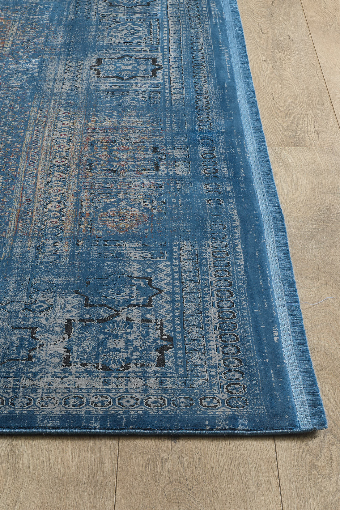 A close-up of the Hidden Treasures Turkish Rug - Azure - 2223B, featuring intricate faded blue, cream, and red motifs on a light wooden floor.