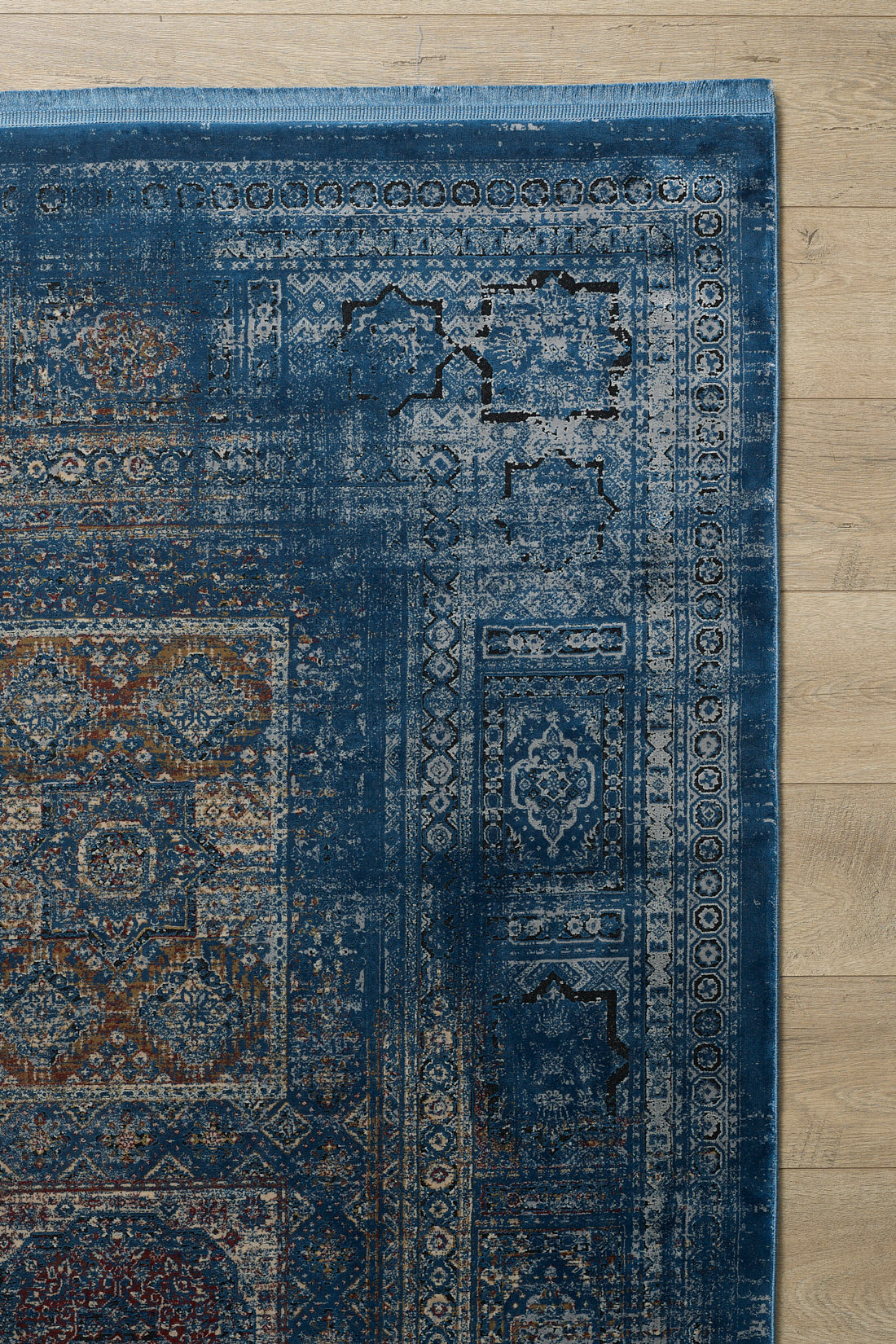 A close-up of the Hidden Treasures Turkish Rug - Azure - 2223B, showcasing its intricate blue, beige, and rust patterns on a light wooden floor. Only part of this modal silk polyester rug is visible.