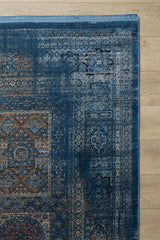 A close-up of the Hidden Treasures Turkish Rug - Azure - 2223B, showcasing its intricate blue, beige, and rust patterns on a light wooden floor. Only part of this modal silk polyester rug is visible.