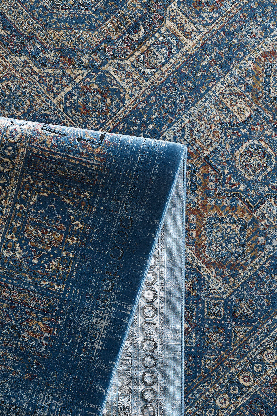 The Hidden Treasures Turkish Rug - Azure - 2223B features intricate blue and beige geometric and floral patterns, with a folded corner displaying the detailed underside.