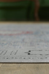 Close-up of the edge of the Hidden Treasures Turkish Rug - Smoky - 2223C, a light-colored, machine-made rug with subtle patterns on a wooden floor. The background is blurred with hints of dark green furniture.