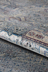A close-up of the Hidden Treasures Turkish Rug - Smoky - 2223C, showcasing intricate blue, gray, white, and red designs with ornate details and a slightly distressed texture.