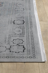 A close-up of the Hidden Treasures Turkish Rug - Smoky - 2223C showcases its gray geometric and circular patterns, thin white fringe, and machine-made quality on a light wooden floor.