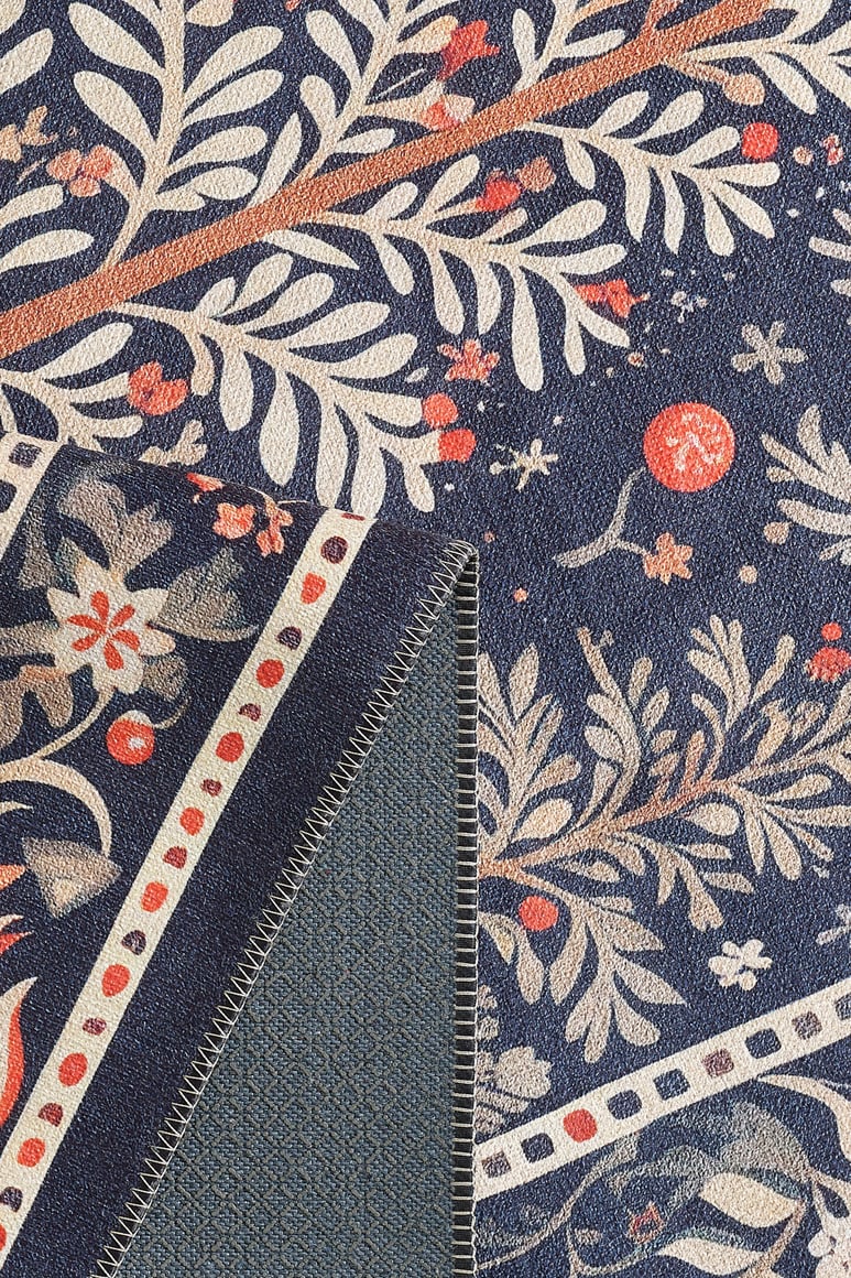 Close-up of the Holiday Heart Washable Area Rug - MDJ001 in blue, featuring a botanical pattern with cream and orange leaves, branches, and red berries. The fold reveals the plain blue underside and detailed edge stitching—ideal for high-traffic areas.