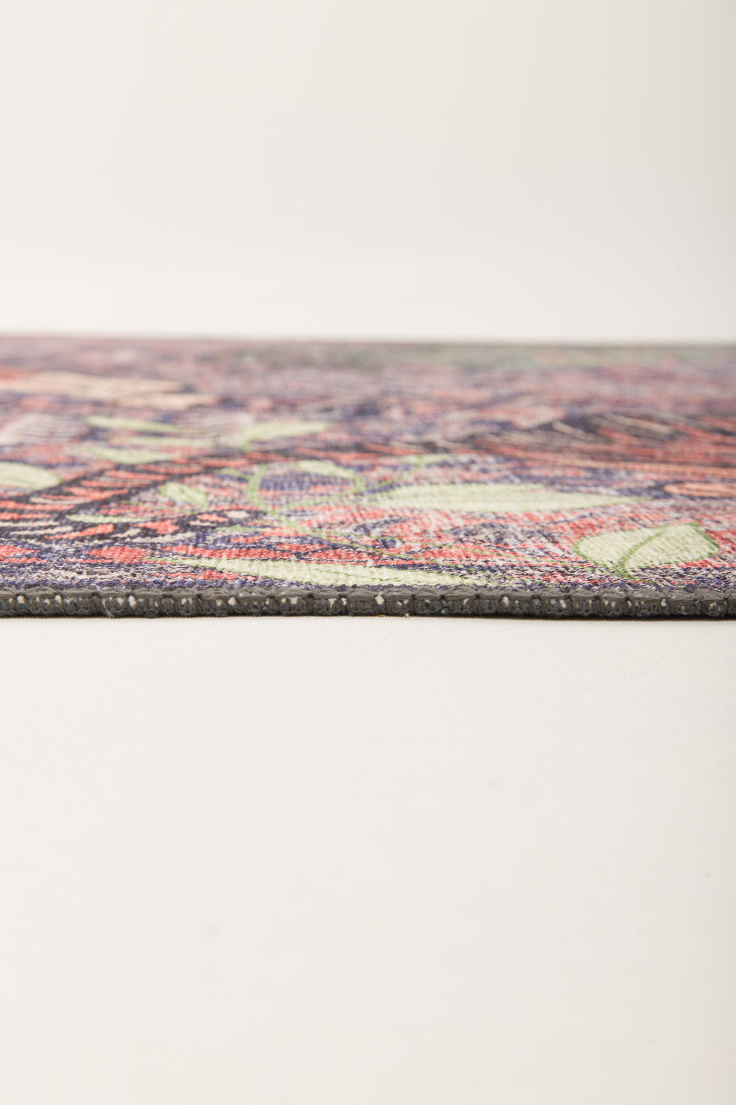 A close-up side view of the Stormstripe Echo - Washable Rug - JR0046 reveals its slim profile, blue tone, and detailed multicolored pattern on a plain light background. The rug lies flat, showcasing its modern texture and contemporary design.