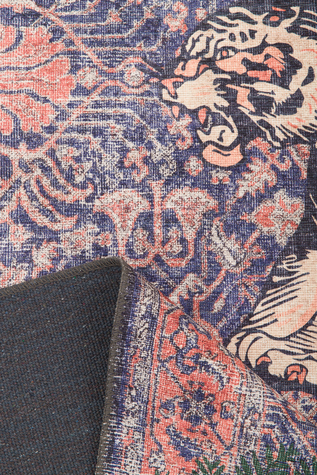 A close-up of the Stormstripe Echo - Washable Rug (JR0046) in blue, featuring an intricate pink and cream floral and tiger design; one corner is folded to show the underside of this washable rug.