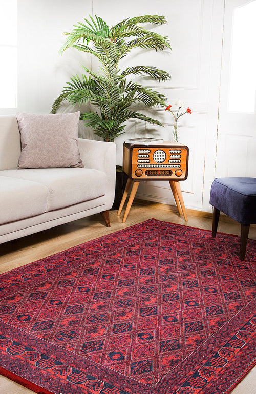 Load image 1 in gallery view. A cozy living room features a beige sofa, purple ottoman, vintage radio on a wooden stand, potted plant, and the Imperial Impressions - Washable Rug - JR1132 (Custom Size)—red and perfect for high-traffic areas. White walls and bright natural light complete the space.