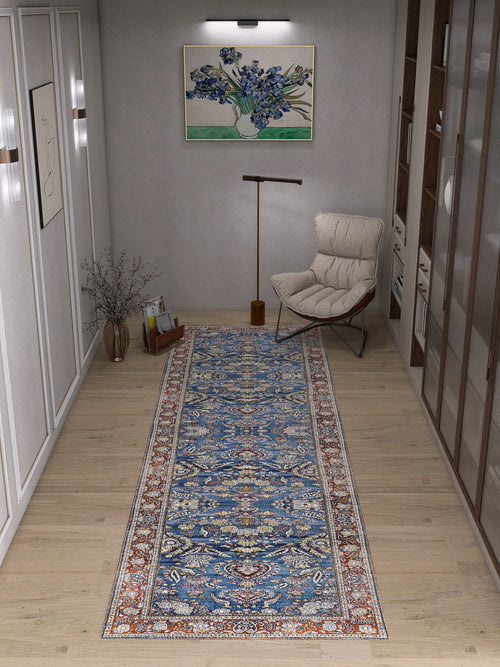 Load image 1 in gallery view. A modern hallway features light wood floors, white paneled walls, the Imperial Medallion - Washable Rug - JRN1006 in blue, a cream lounge chair, floor lamp, glass vase with branches, and a framed floral painting.