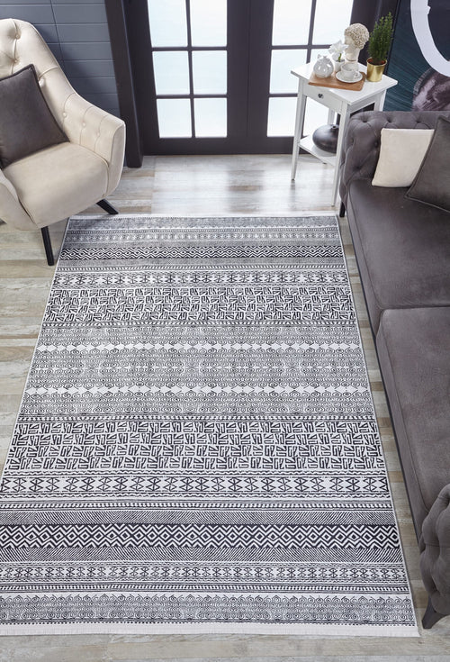 Load image 1 in gallery view. A living room featuring the Indie Impressions - Washable Rug - JR1648 (Custom Size) in gray-anthracite, a beige armchair, gray sofa, white side table with plants and decor, and large glass doors allowing natural light in.