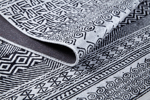 Load image 1 in gallery view. A close-up of the Indie Impressions - Washable Rug - JR1648 (Custom Size) in gray-anthracite, featuring intricate black geometric and spiral designs on a light background, with its edge folded to show both sides of the textile.