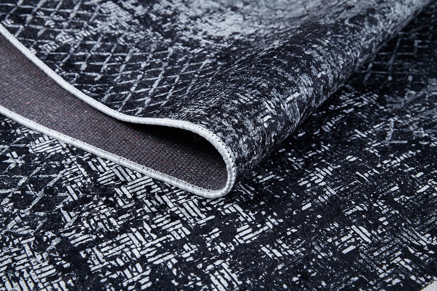 A close-up of the Infinity Garden - Washable Rug - JR1749 (Custom Size), featuring black and white abstract geometric patterns, ideal for high-traffic areas. It’s shown slightly folded to reveal the underside and detailed edge stitching.