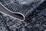 A close-up of the Infinity Garden - Washable Rug - JR1749 (Custom Size), featuring black and white abstract geometric patterns, ideal for high-traffic areas. It’s shown slightly folded to reveal the underside and detailed edge stitching.