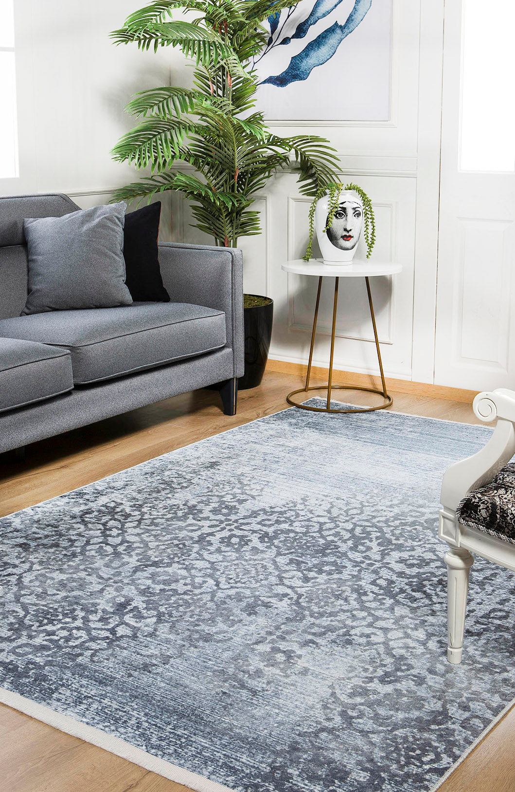 A modern living room featuring a gray sofa, leafy potted plant, round side table with a decorative vase, white accent chair on light wood flooring, and the allergy-friendly Intricate Scroll - Washable Rug - JR342 (Custom Size)—ideal for high-traffic areas.