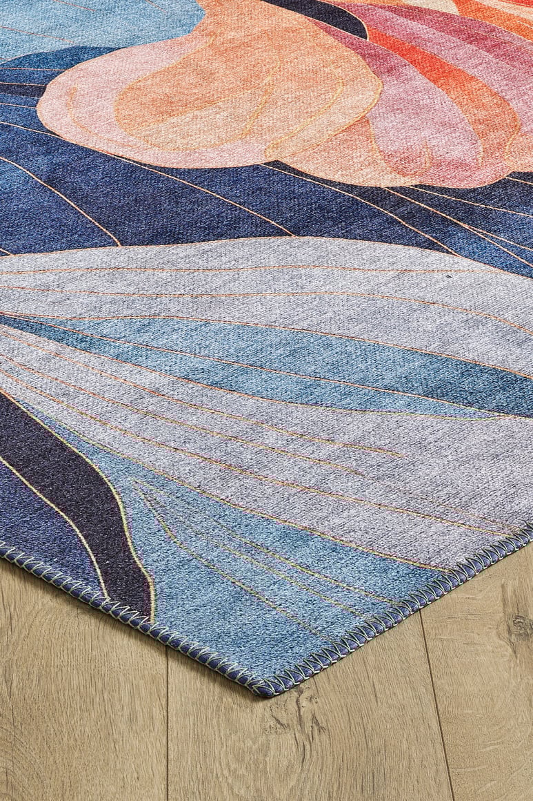 A close-up of the Iris Abstract Floral Washable Rug - MDJ009, featuring abstract shapes in blue, pink, orange, and peach on a light wood floor, with visible stitched edges and a soft, textured look.