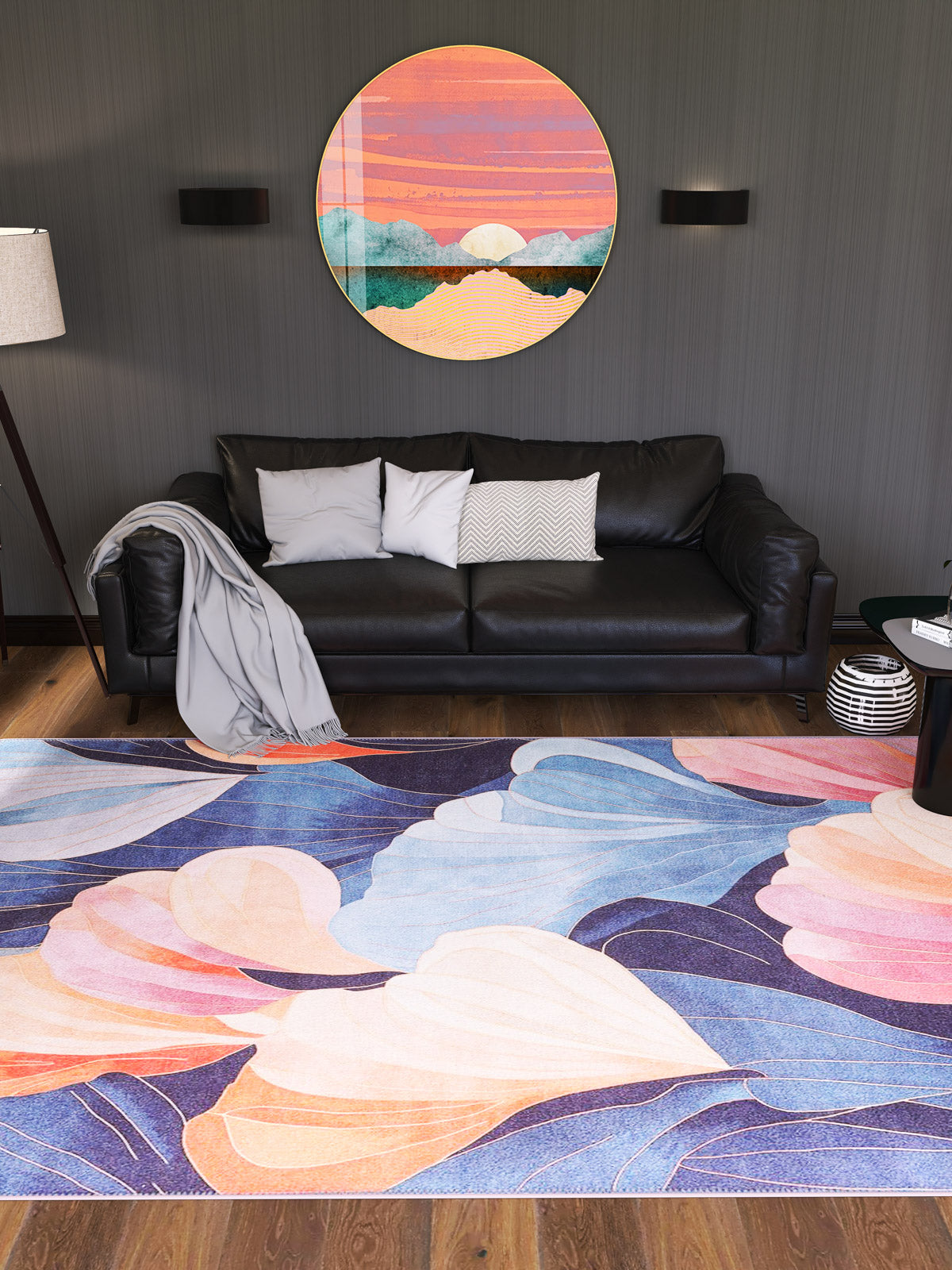 A modern living room features a black sofa, gray throw and cushions, round sunset wall art, two black wall lights, a floor lamp, books on a small round side table, and the Iris Abstract Floral Washable Rug - MDJ009 (Custom Size), perfect for high-traffic areas.