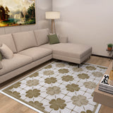 A modern living room features a beige sectional sofa with green pillows, a floor lamp, landscape painting, and the Ivory Clover - Washable Rug - JRS014 with a large green and brown floral design—perfect for high-traffic areas. A small plant sits in the corner.