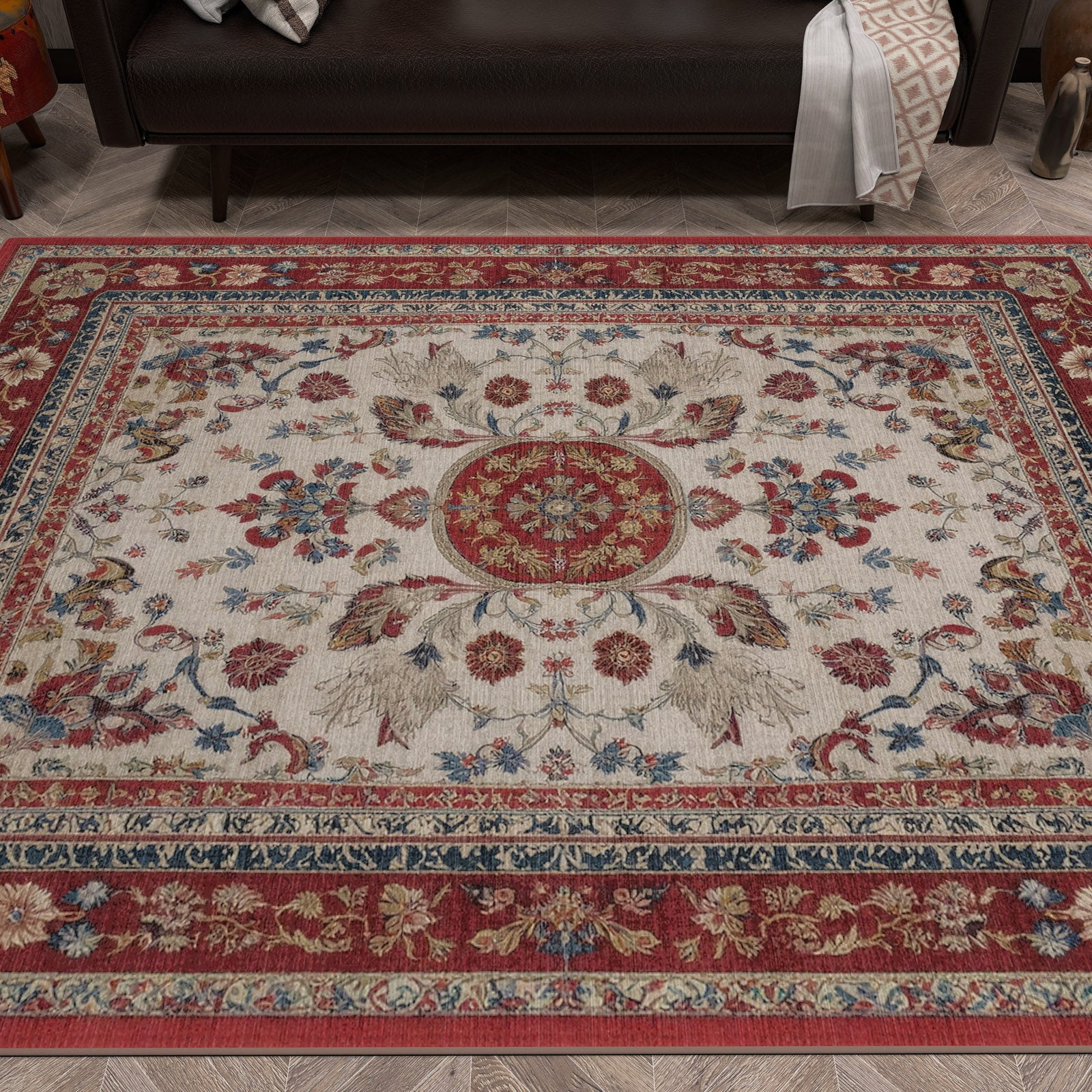The Imperial Rose - Washable Rug - JRS023, with a red, cream, and blue floral medallion design and ornate borders, is laid on a wooden floor in front of a dark sofa.