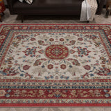The Imperial Rose - Washable Rug - JRS023, with a red, cream, and blue floral medallion design and ornate borders, is laid on a wooden floor in front of a dark sofa.