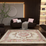 A cozy living room with a dark sofa, pink and white cushions, and a gray throw. The Petal Mist - Washable Rug - JRS025 with a pink and beige geometric pattern brightens the wooden floor. Shelves, soft lighting, wall art, and a plant complete the look.