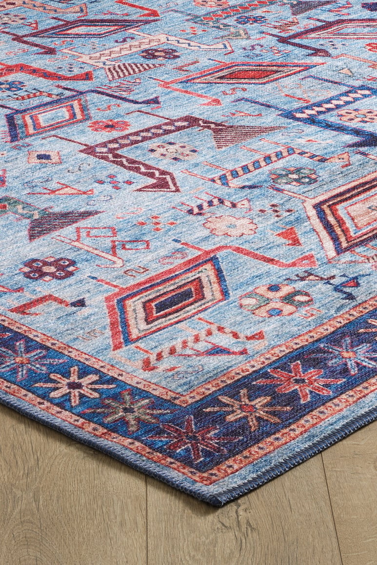 A corner of the Birdwatcher's Dream Blue Washable Rug - LCC3020, featuring geometric patterns in red, cream, and dark blue with a decorative border on a light wood floor—ideal for high-traffic areas.