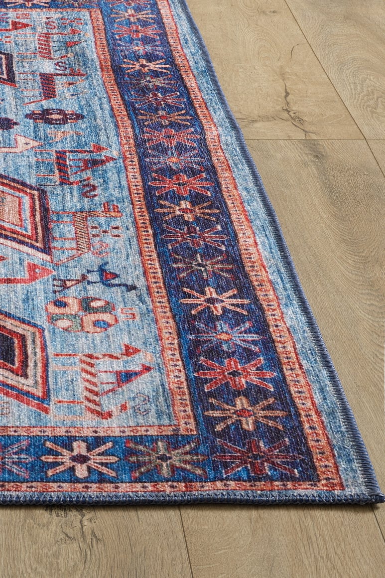 A close-up of the Birdwatcher's Dream Blue Washable Rug - LCC3020, featuring vibrant geometric and floral patterns in blue, red, and cream on a light wooden floor—perfect for high-traffic areas.