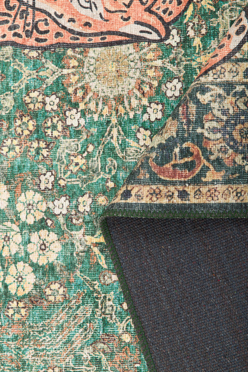 Bild 1 in Galerieansicht laden. A close-up of the Jungle Ember - Washable Rug - JR0047, a colorful vintage-style green rug with cream and orange tones. One corner is folded to show the dark backing and detailed geometric front pattern.