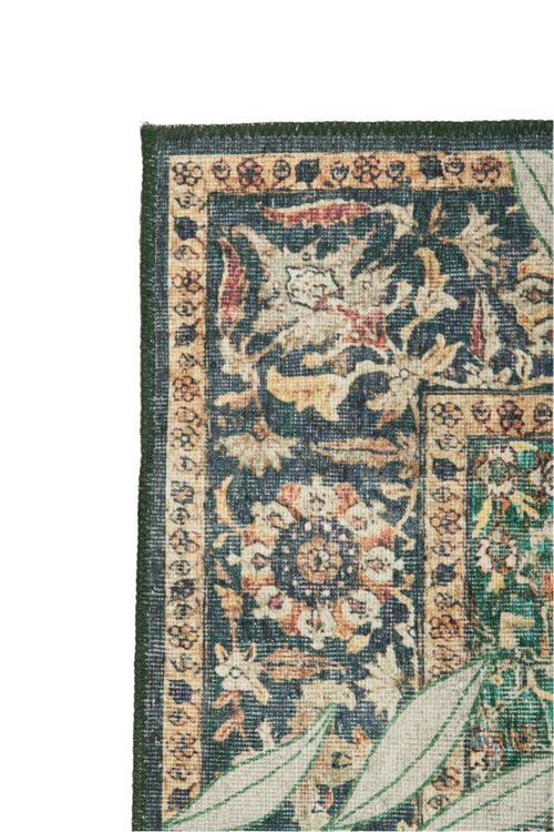 Bild 1 in Galerieansicht laden. Close-up of the Jungle Ember - Washable Rug (JR0047): ornate, vintage-style with a dark floral pattern, green border, and cream background. Large light green leaves partially cover its edge.
