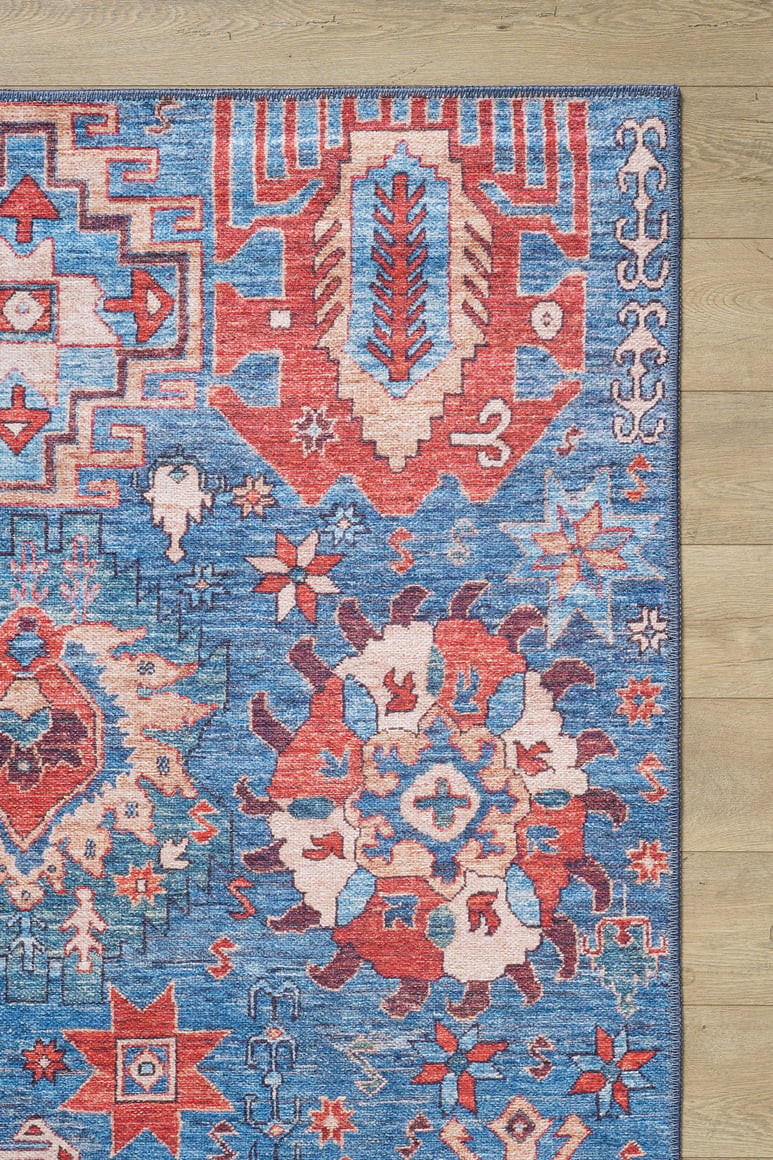 The Kaleidos Authentic Blue Washable Rug - LCC3028 features intricate geometric and floral patterns in red, blue, white, and beige. Only the top right corner of this colorful rug is visible on a light wood floor—ideal for high-traffic spaces.