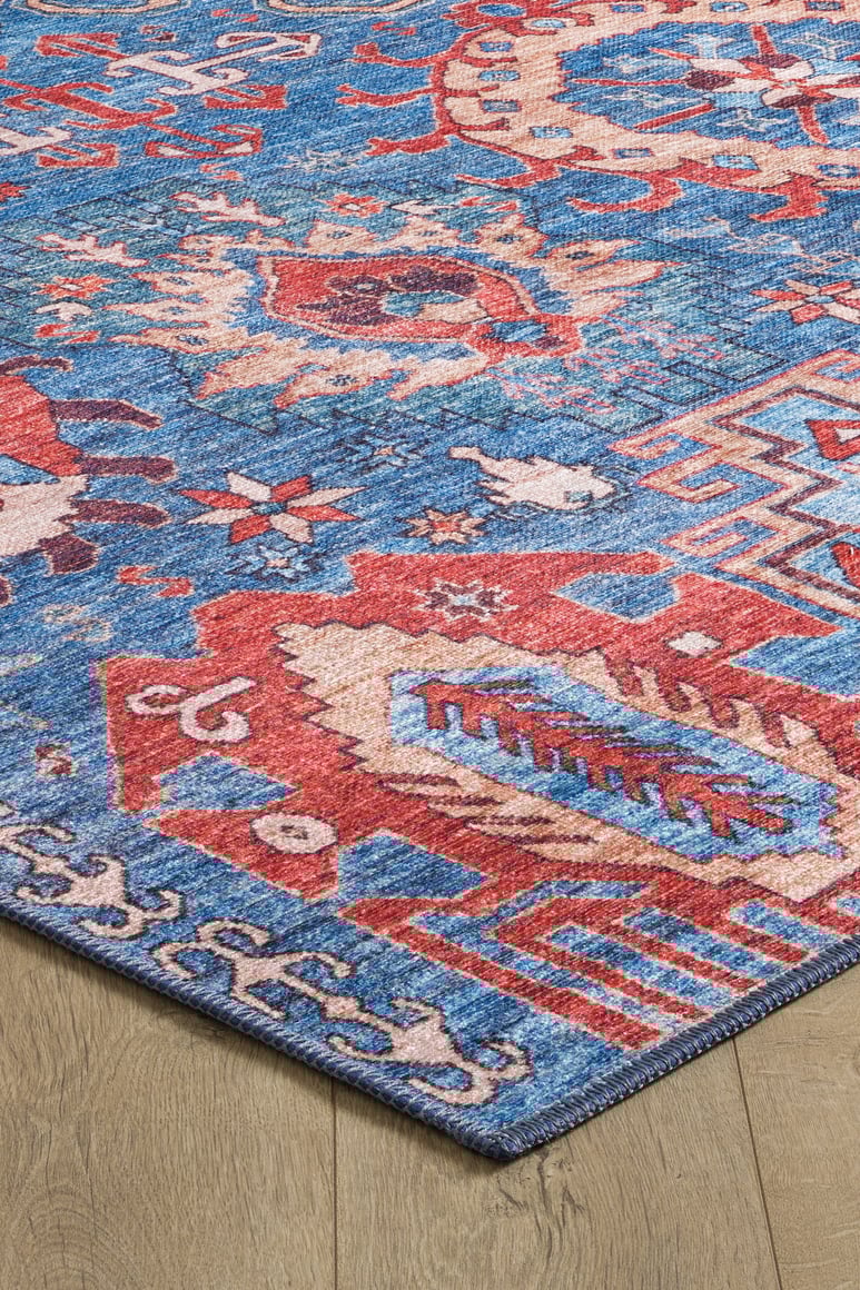 A close-up of the Kaleidos Authentic Blue Washable Rug - LCC3028, featuring bold geometric and abstract patterns in red, blue, and beige on a light wooden floor—ideal for high-traffic areas.