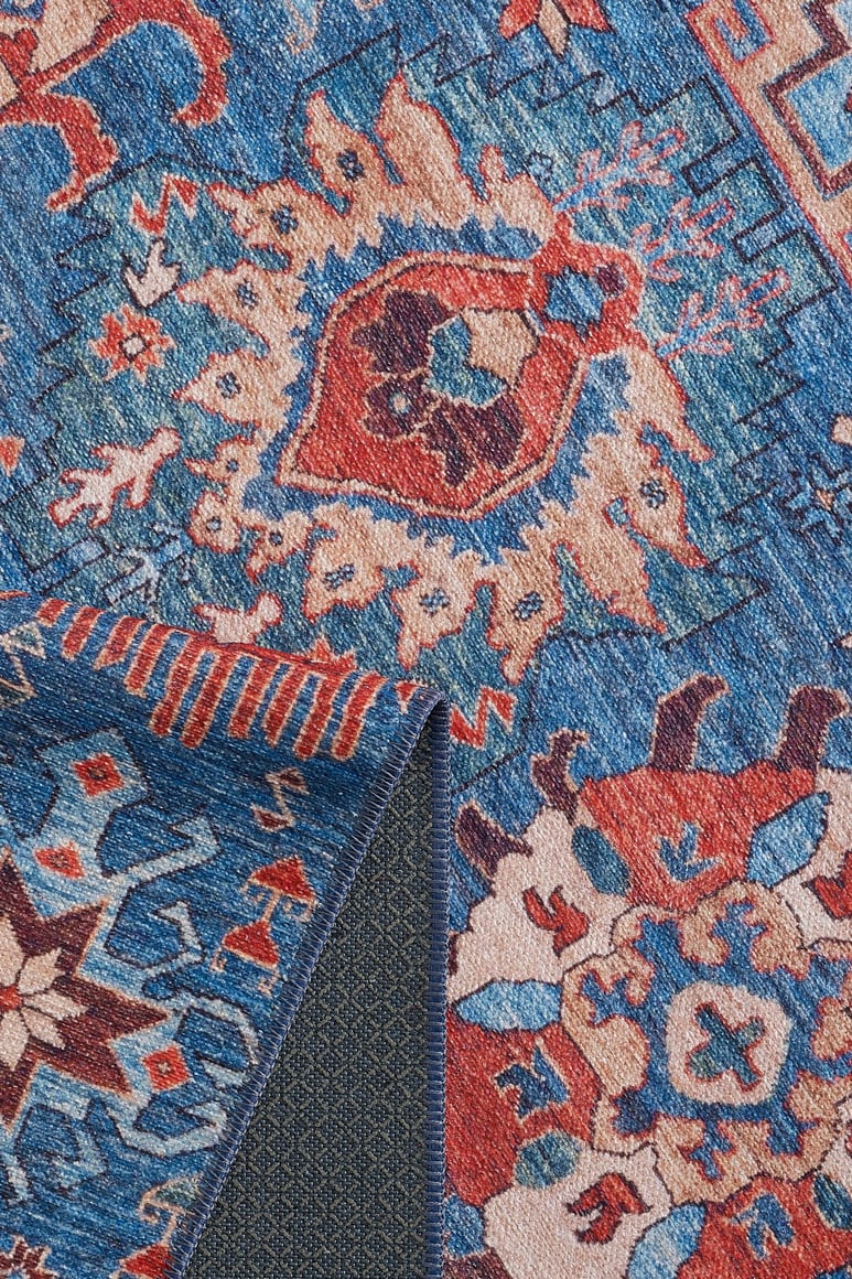 A close-up of the Kaleidos Authentic Blue Washable Rug - LCC3028 shows its intricate geometric and floral patterns in red, cream, and gold. A folded corner reveals the textured backing—ideal for high-traffic spaces or easy cleaning.