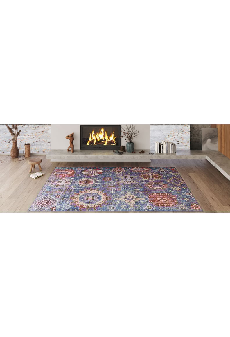 A cozy living room with a lit fireplace, modern decor, and the Kaleidos Authentic Blue Washable Rug - LCC3028 (Custom Size) featuring colorful patterns on a light wooden floor—ideal for high-traffic spaces. Decorative vases and sculptures line the mantel.