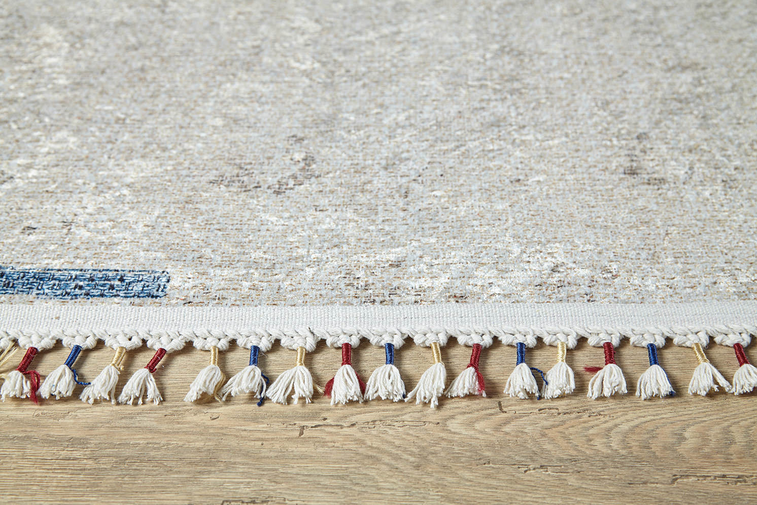 Close-up of the Kaleidoscope Dreams - Washable Rug - JR5055 (Custom Size), light-colored with white, red, and blue tassels on a wooden floor. Subtle, faded pattern—ideal for high-traffic or allergy-sensitive areas.