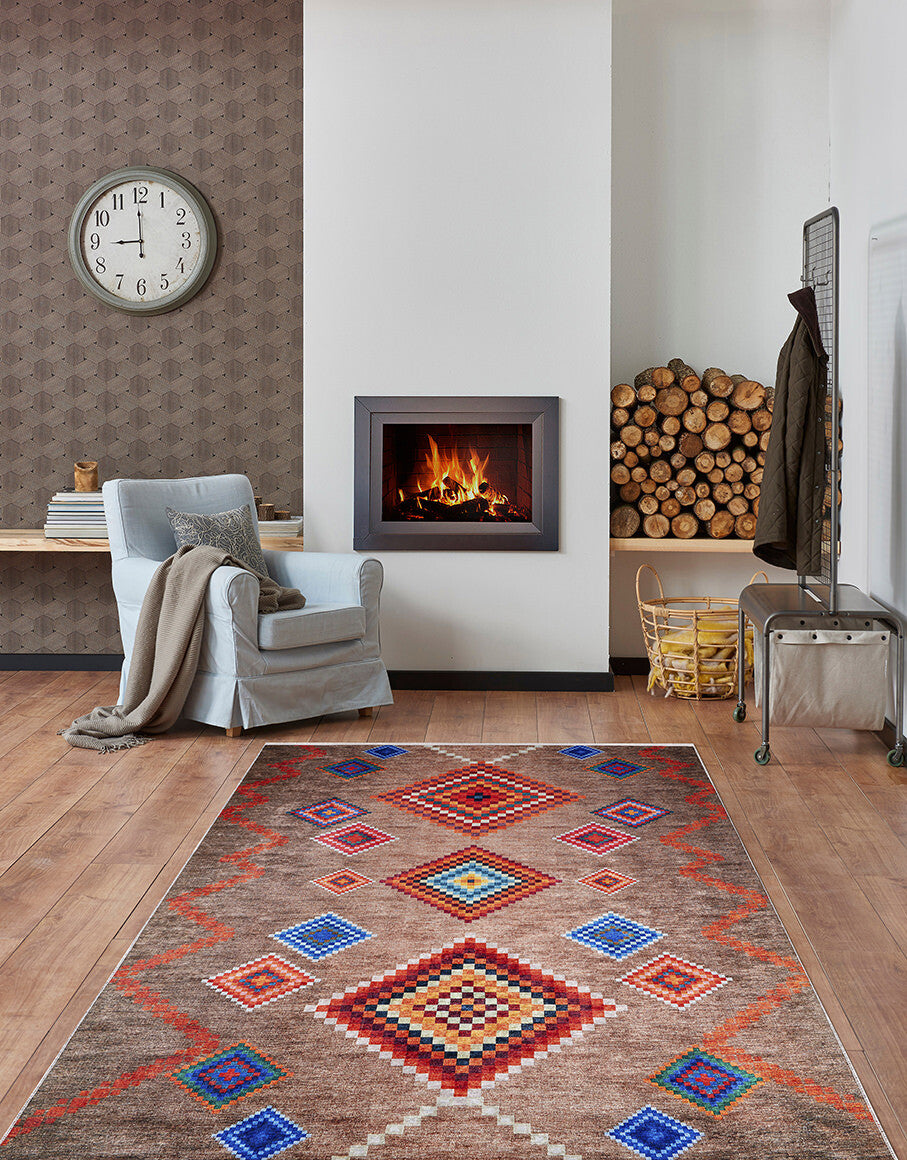 A cozy living room with the Kilim Kingdom - Washable Rug - JR1536 (Custom Size), gray armchair with blanket, wall clock, fireplace, stacked firewood, and wooden floors. The warm modern-rustic decor is perfect for high-traffic areas.