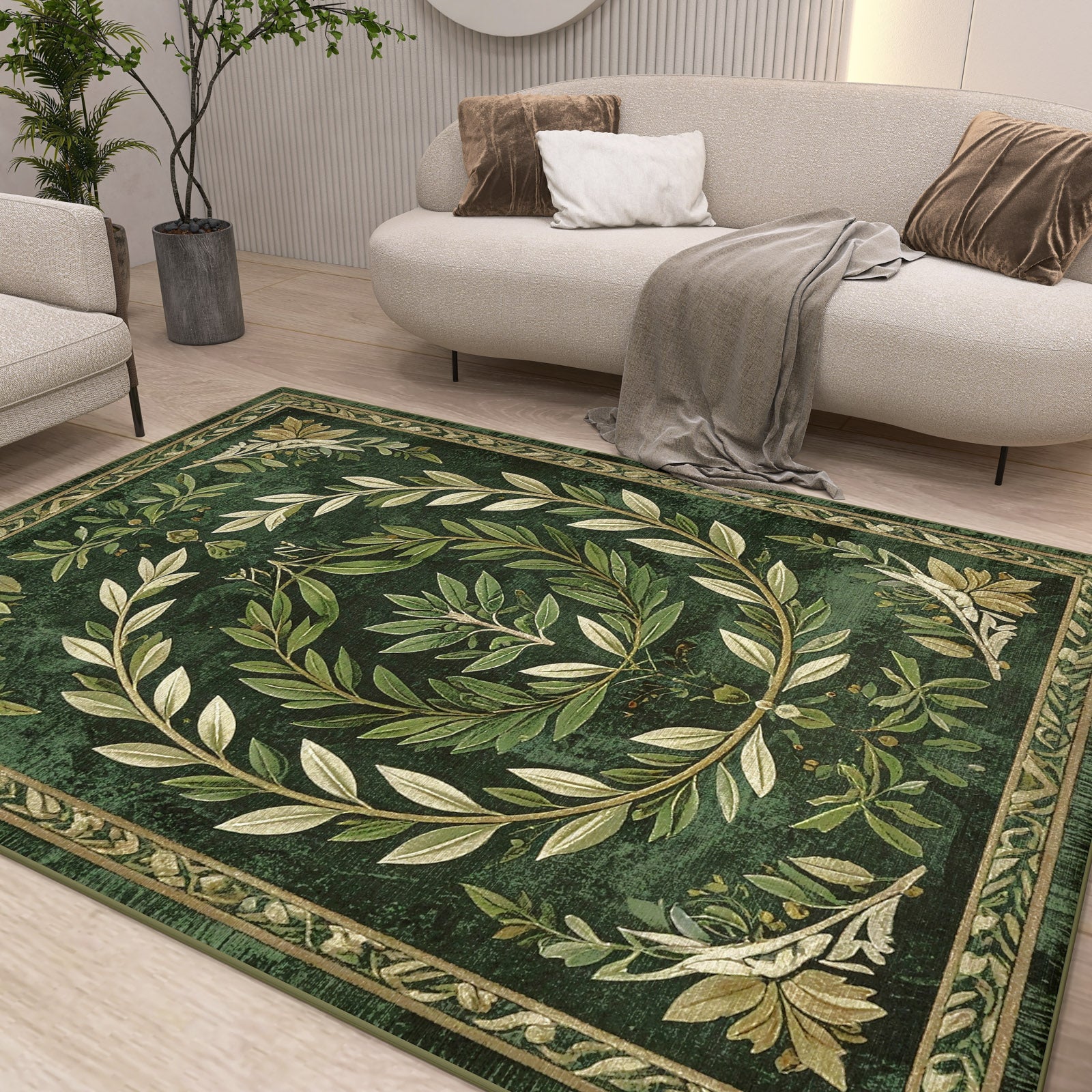 A modern living room with a white sofa, neutral cushions, and a gray throw features the Laurel Crown - Washable Rug - JRS024, showcasing an ornate olive leaf wreath and subtle geometric pattern. Plants and minimal decor complete the cozy, elegant space.