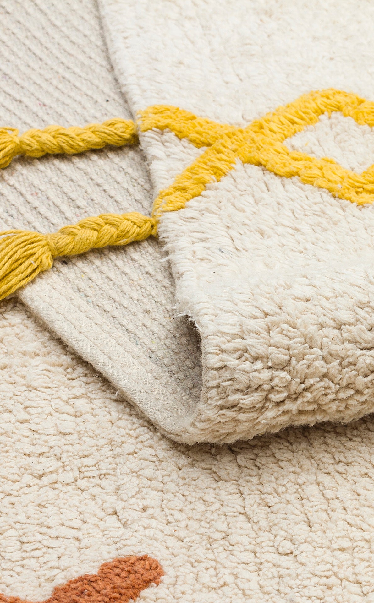 A close-up of the Little Dream - Washable Shaggy - CBN12 rug, featuring cream and yellow geometric patterns with thick, twisted yarn details—its soft, washable texture and folded edge make it ideal for adding comfort to a kids’ room.