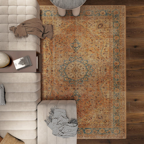 Load image 1 in gallery view. A top-down view of a living room featuring a beige tufted sofa, the Classic Laurel - Washable Rug - JRN1022 in orange and blue, a coffee table, side table with books, and a black-and-white throw blanket on the sofa.