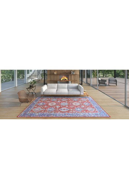 Load image 1 in gallery view. A modern living room features a white sofa, a lit fireplace in a wooden wall, a woven chair, and the Lunavale Red Blue Washable Rug - LCC3007 with colorful patterns on light wood floors, with large windows showcasing trees outside.